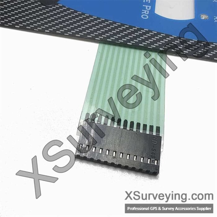 A close-up view of a green ribbon cable attached to a black electronic connector component, positioned below a blue and black device panel.